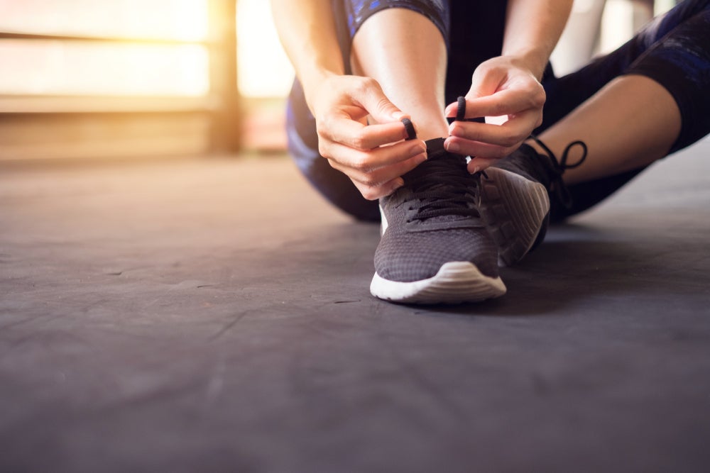 woman tying workout shoes on the ground for 24/7 workout