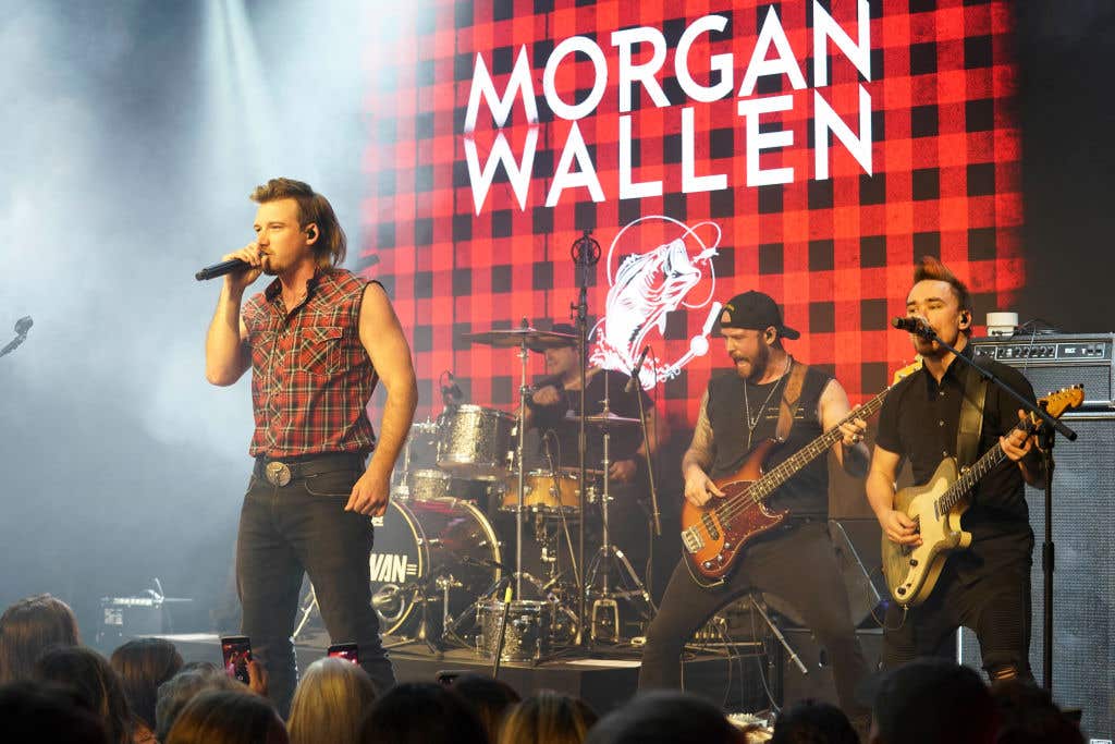 Morgan Wallen singing on stage with his band his name on the back wall