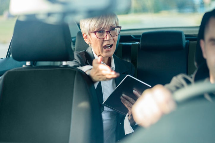 Nervous senior female manager riding on a back seat of a car, running late for a meeting