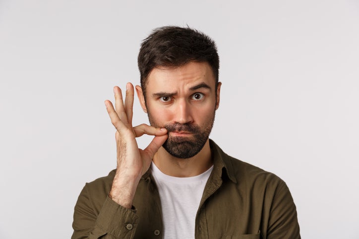 My lips are sealed with promise. Serious and funny bearded adult man keep mouth shut, making zip gesture and raise one eyebrow as hinting person stay silent, keep secret safe, white background