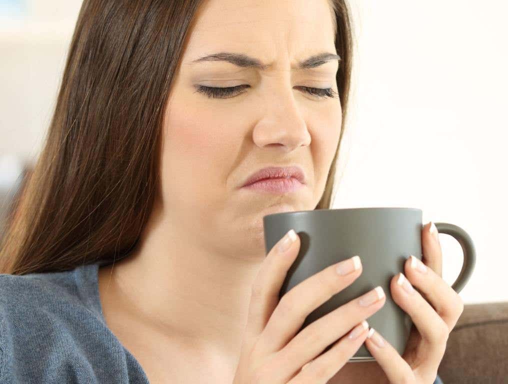 Woman looking disgusted at cup of coffee (consider coffee alternatives)