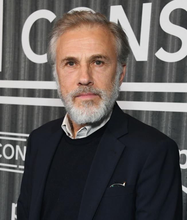 Christoph Waltz attends Prime Video's "The Consultant" Los Angeles Premiere with grey hair wearing a black shirt and black jacket.