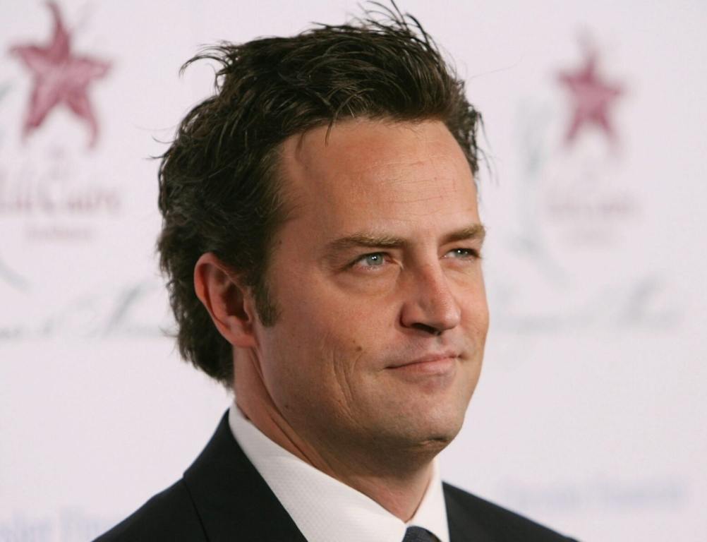 Matthew Perry arrives at the 9th Annual Dinner Benefiting the Lili Claire Foundation smiling facing right wearing a suit and tie.