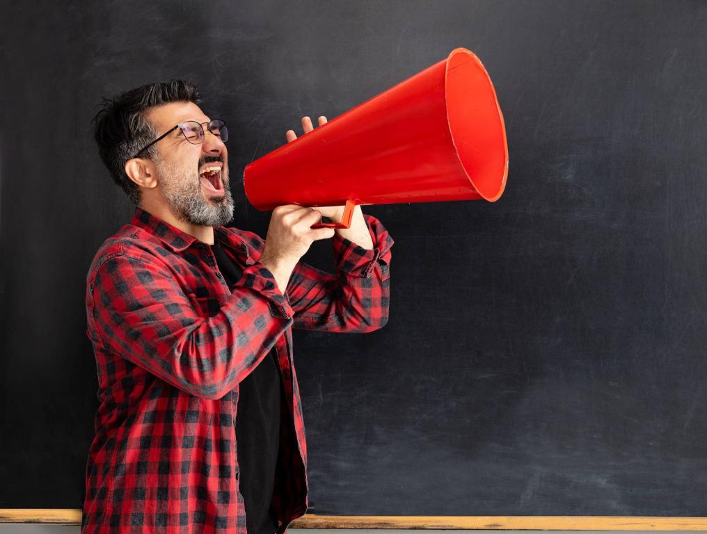 A man holding a red megaphone standing in front of a chalkboard.