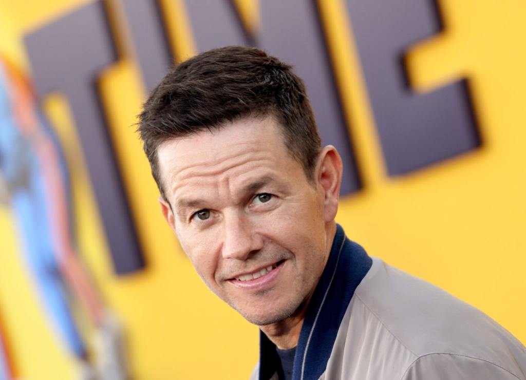 Mark Wahlberg attends the Los Angeles premiere of Netflix's "Me Time" smiling turned left facing center wearing a beige jacket.