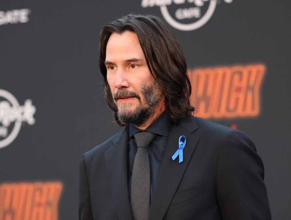 Keanu Reeves attends the Los Angeles Premiere of Lionsgate's "John Wick: Chapter 4" facing left wearing a black suit with blue ribbon.