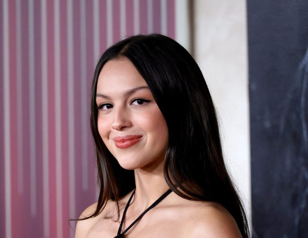 Olivia Rodrigo attends "The Hunger Games: The Ballad Of Songbirds & Snakes" Los Angeles Premiere smiling facing right wearing a strappy black dress.