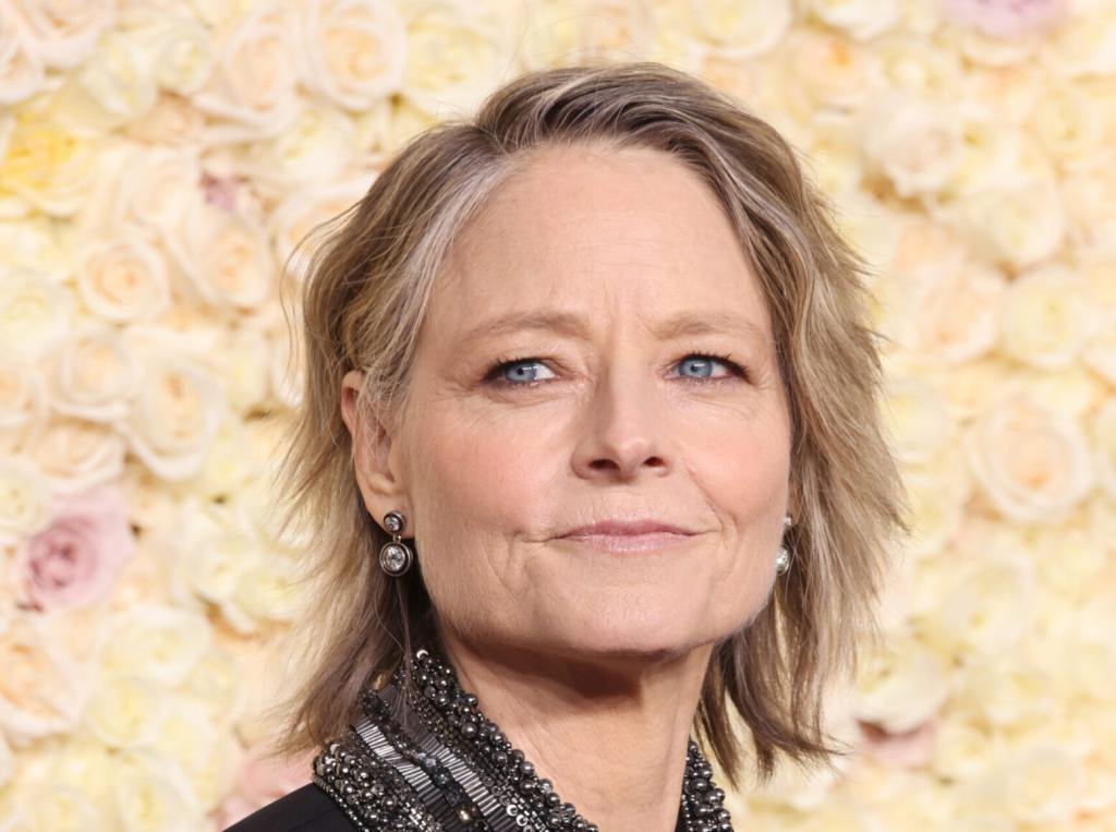 Jodie Foster attends the 81st Annual Golden Globe Awards smiling looking left wearing a bedazzled grey scarf.