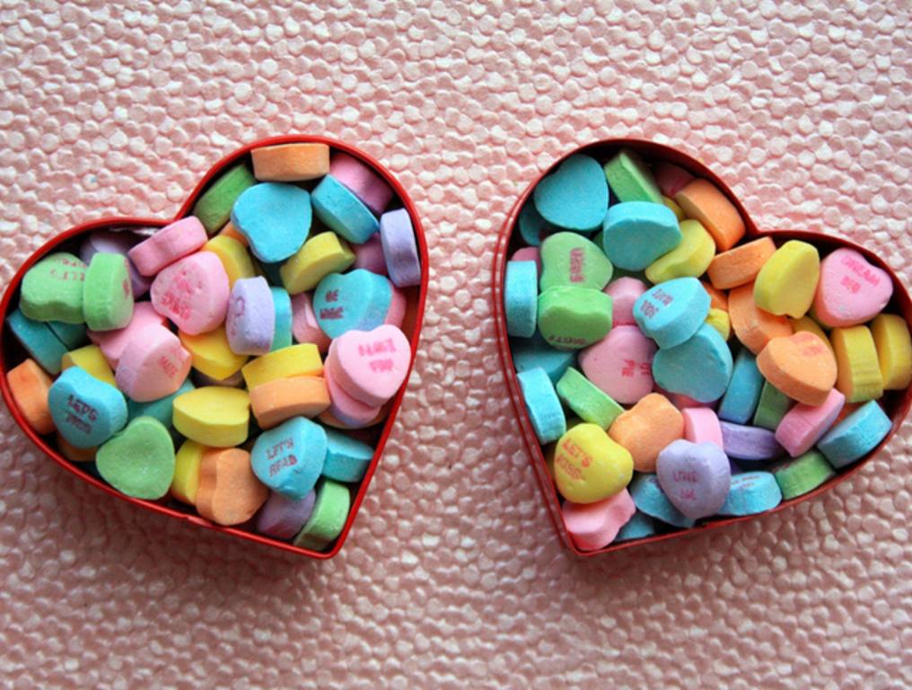 two hearts and candy conversation hearts on pink background