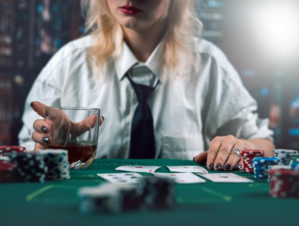 attractive girl in shirt and hat drinking whiskey and looking at poker cards in casino. girl player makes a bet. poker in the casino