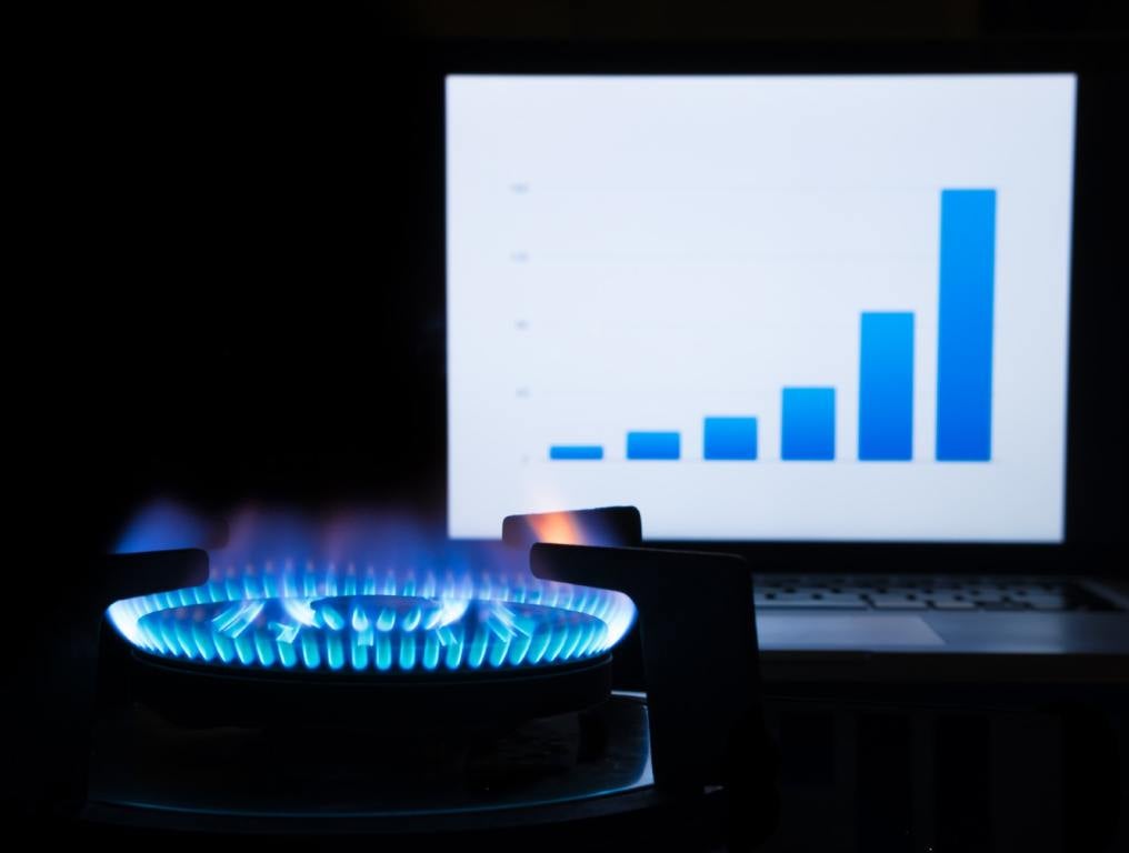 Many Southern Nevadans are shocked and dismayed by higher gas bills. Photo of a gas burner on high, in a dark room with a black background. Right behind the gas burner with the blue flame is a computer screen. On the computer screen is a blue bar graph on a white background, with the blue bars getting higher from left to right.