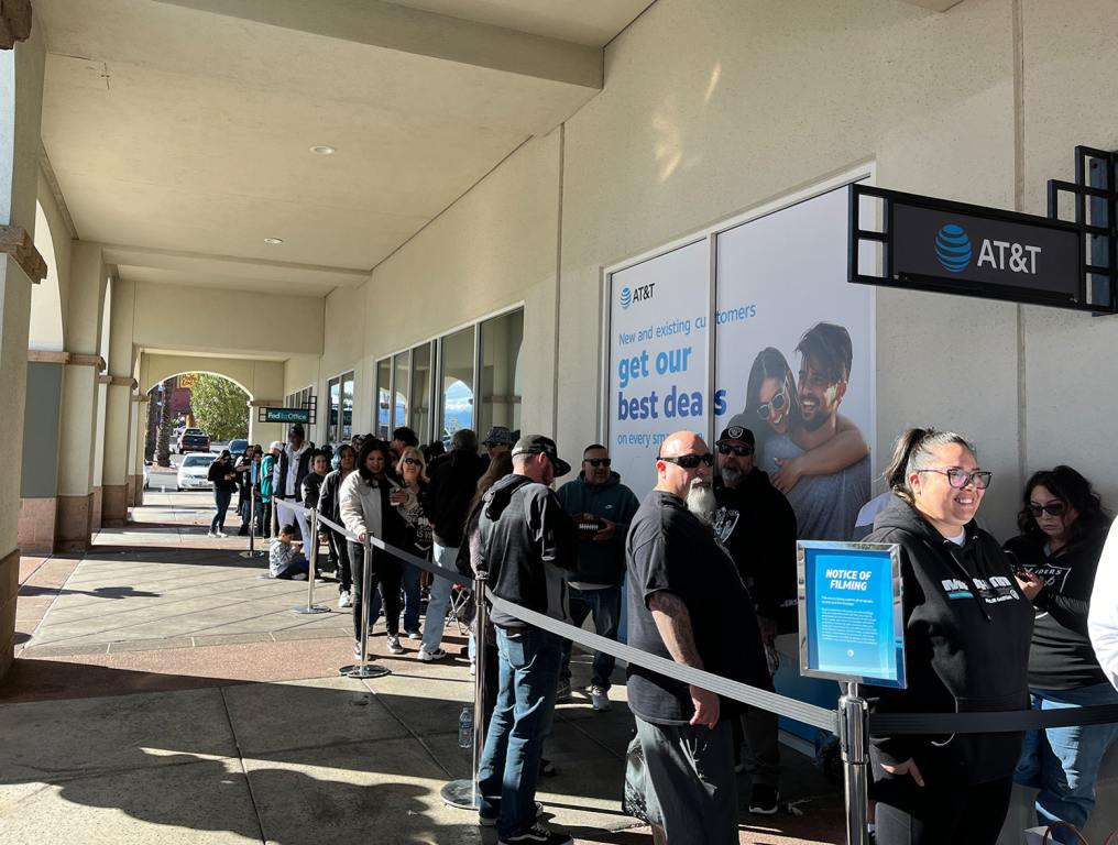 A bunch of people wait in a line along a building wall.