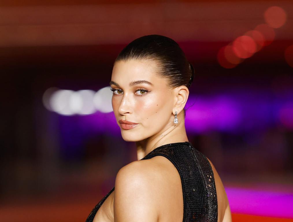 Hailey Bieber attends the Academy Museum of Motion Pictures 3rd Annual Gala looking back wearing a sleeveless black gown with her hair in a tight bun.