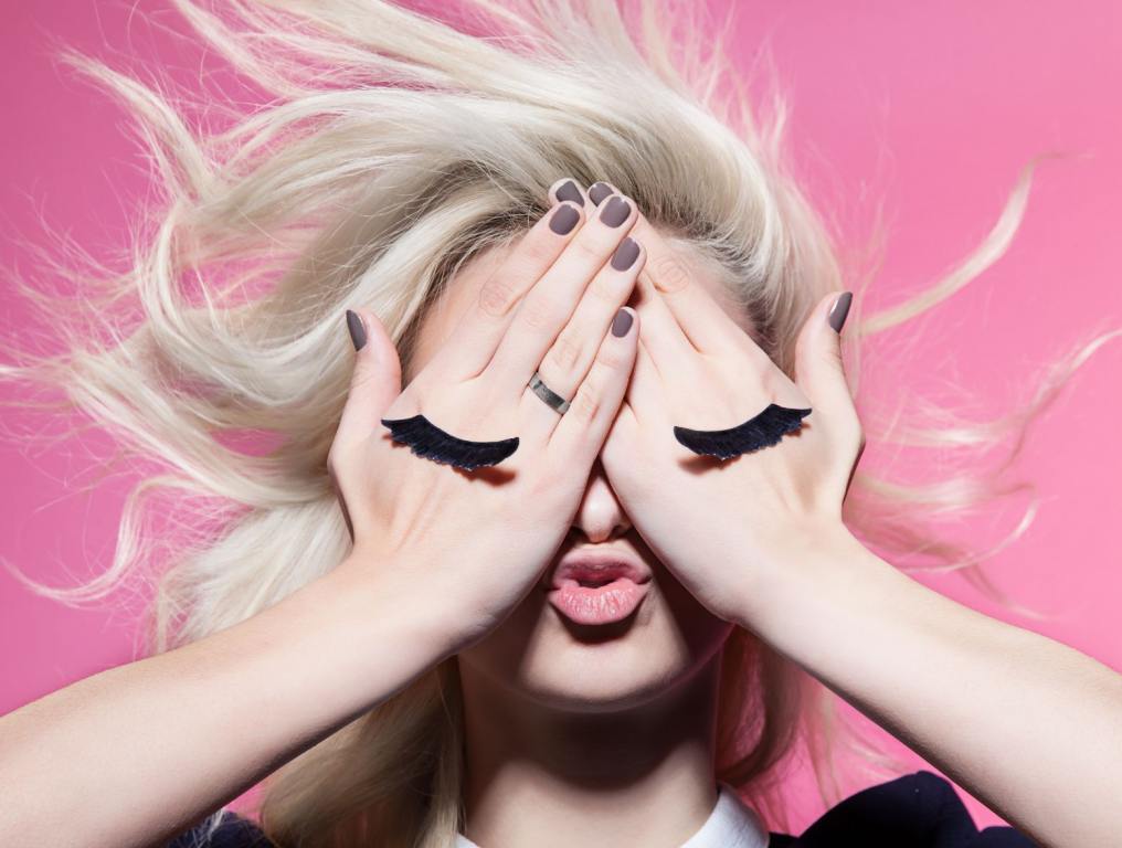 Girl with hands over her face with fake eyelashes on the front of her hands