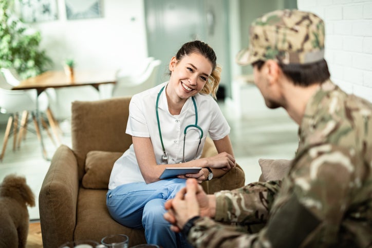 Happy nurse using touchpad and communicating with a soldier while visiting him at home.