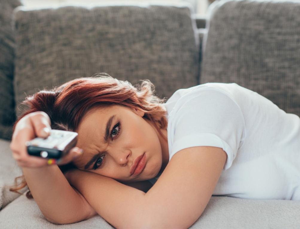 Angry girl with remote controller watching tv at home