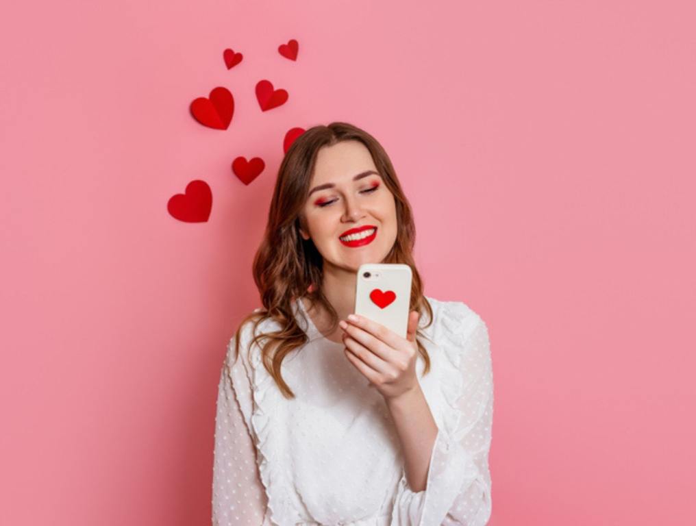 Dating App, Dating Profile. The girl reads love sms smiling on a pink background.