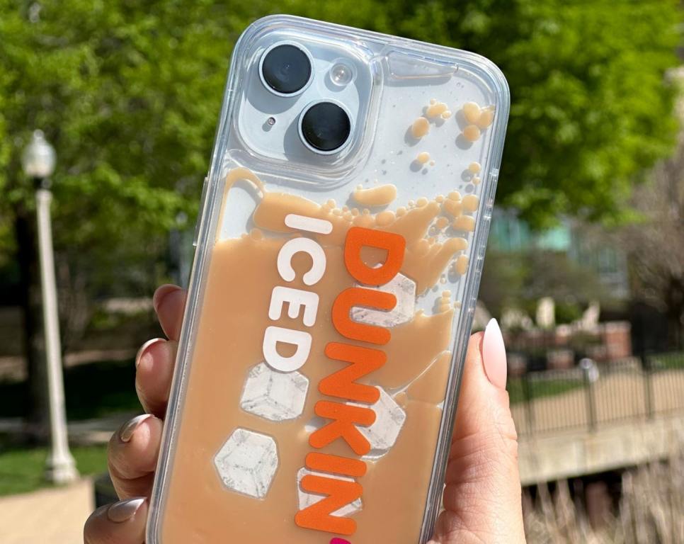 The Dunkin' Iced Coffee iPhone case being held in the air next to a green tree