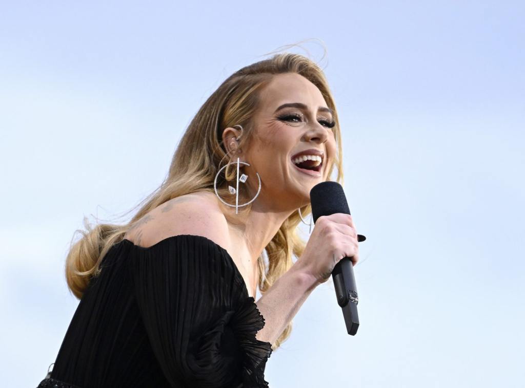 Adele performs on stage as American Express present BST Hyde Park smiling singing facing left wearing a black off-shoulder gown, Adele’s Adorable Moment With Mini-Me Fan During Las Vegas Show.