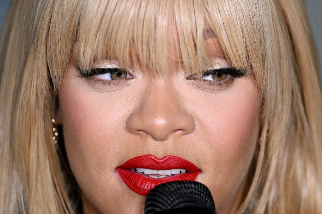 Rihanna attends the FENTY x PUMA Creeper Phatty Earth Tone Launch Party in a super-close up photo of her face with red lipstick and blonde bangs with a microphone held up to her mouth as she looks to the right, Rihanna Sparks Music Retirement Rumors.