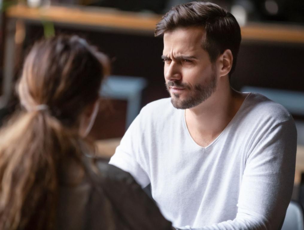 Man and woman sitting at table, man has confused faced, social etiquette concept.