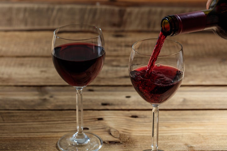 2 red wines under $10 poured in glasses on a wood table.