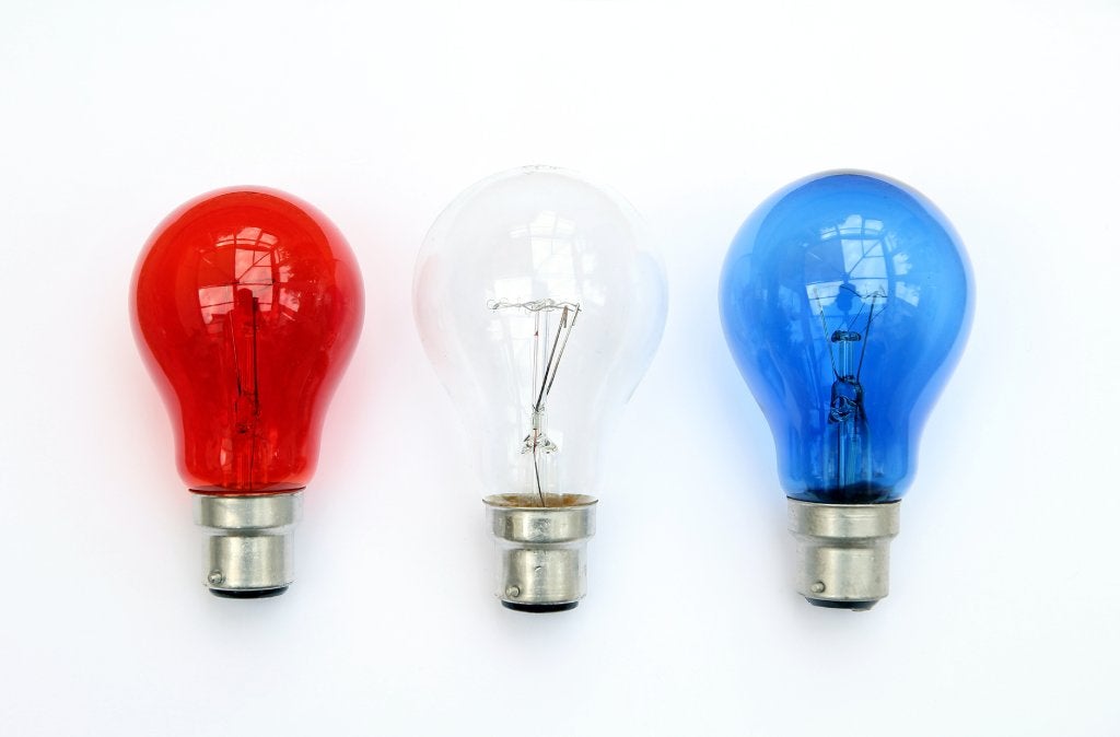 Three light bulbs in a row lay on a white background. The first is red, the middle white and the last one is blue.