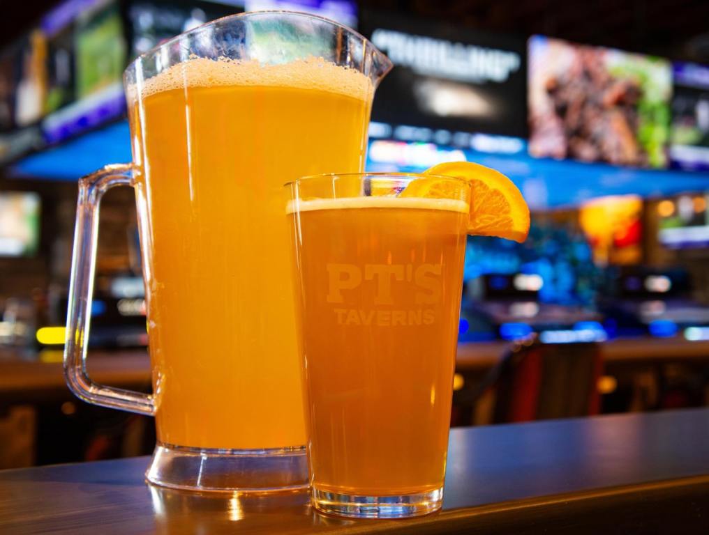 A pitcher of beer sits on a bar behind a pint of beer with an orange slice. Concept: Las Vegas taverns.