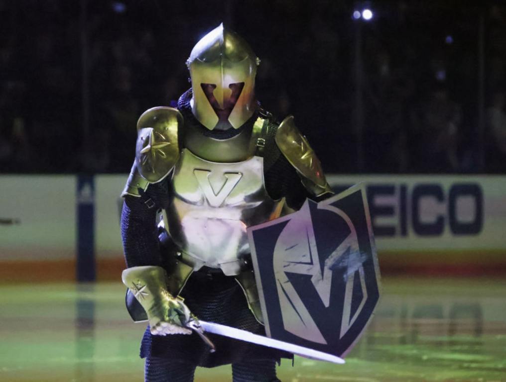 The Vegas Golden Knights have earned another "Stanley" Award for best Game Presentation. Photo of Lee Orchard as the Golden Knight during pregame entertainment prior to Game Two of the 2023 Stanley Cup Finals at T-Mobile Arena. The arena lights are down and there are lasers which shade the ice a bright green. Orchard is wearing his Golden Knight costume complete with shield featuring the Vegas "V" logo, a sword, a helmet with the "V" logo cut into the facemask, and armor similar to that worn by warriors during the middle ages.