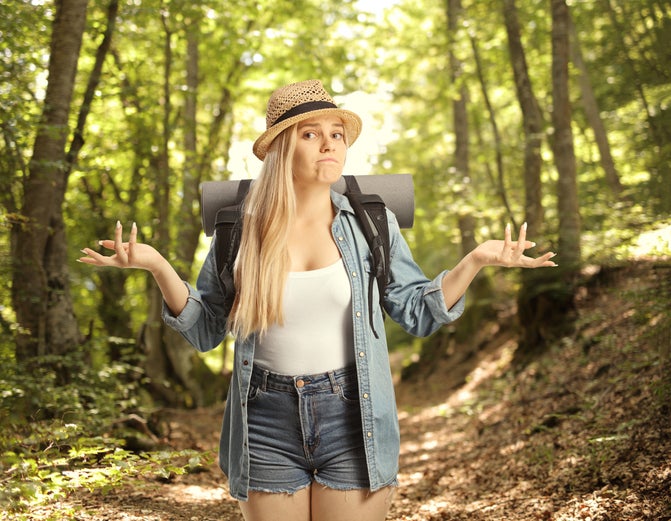 Confused female backpacker gesturing with hands and wondering what to do in a middle of a forest