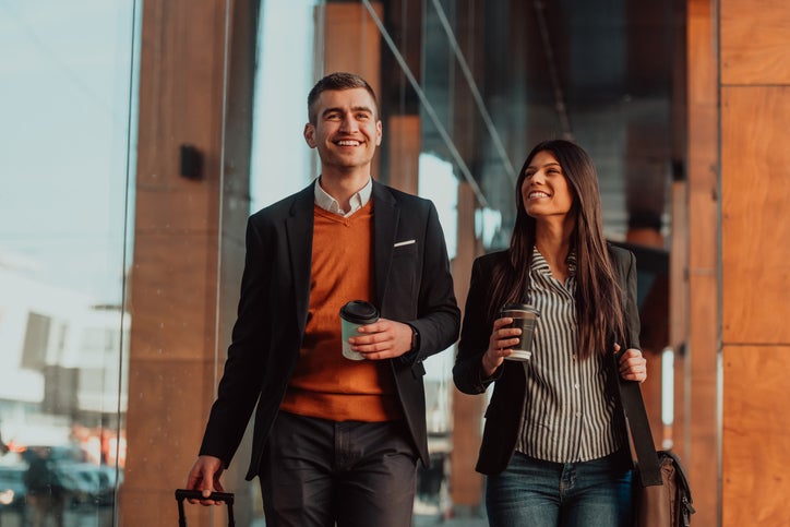 Businessman and businesswoman talking and holding luggage traveling on a business trip, carrying fresh coffee in their hands. Business concept. High-quality photo