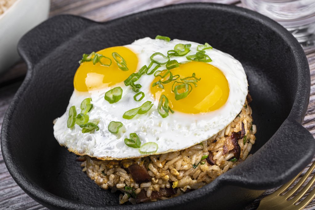 A black skillet with bacon fried rice topped with a sunny-side-up egg and green onions.