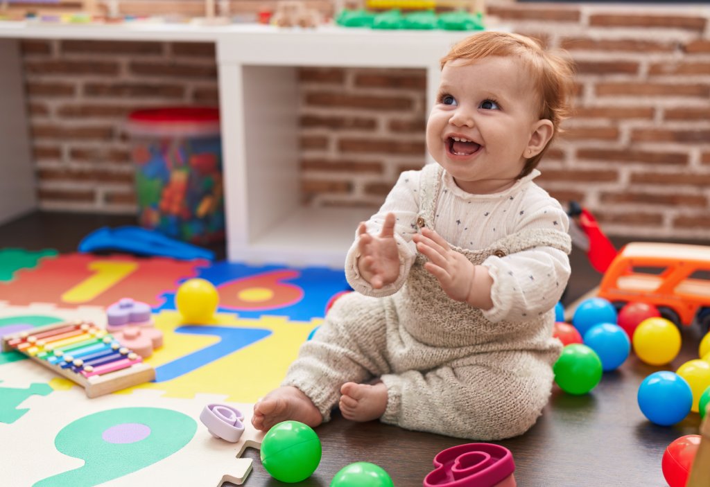 Happy baby is sitting on the floor playing with various rainbow-colored toy.